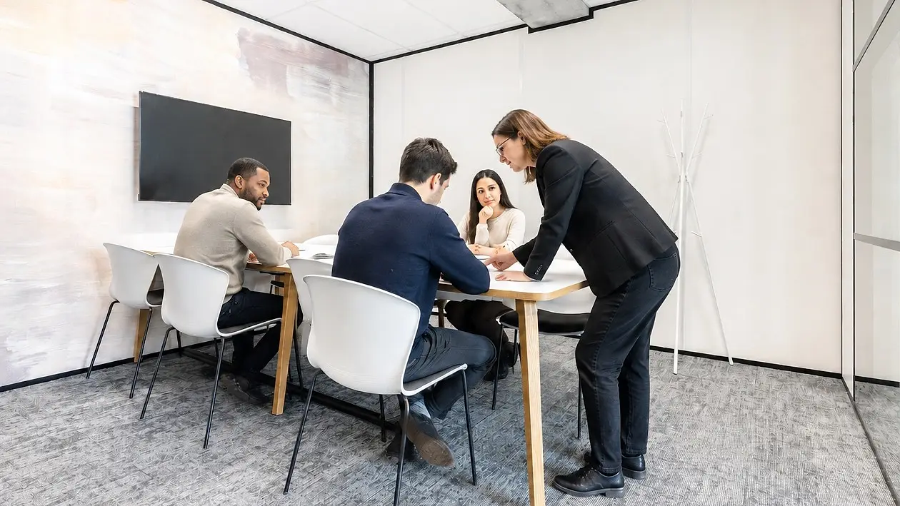 Une formatrice penchée sur un dossier avec trois participants, autour d'une table de travail.