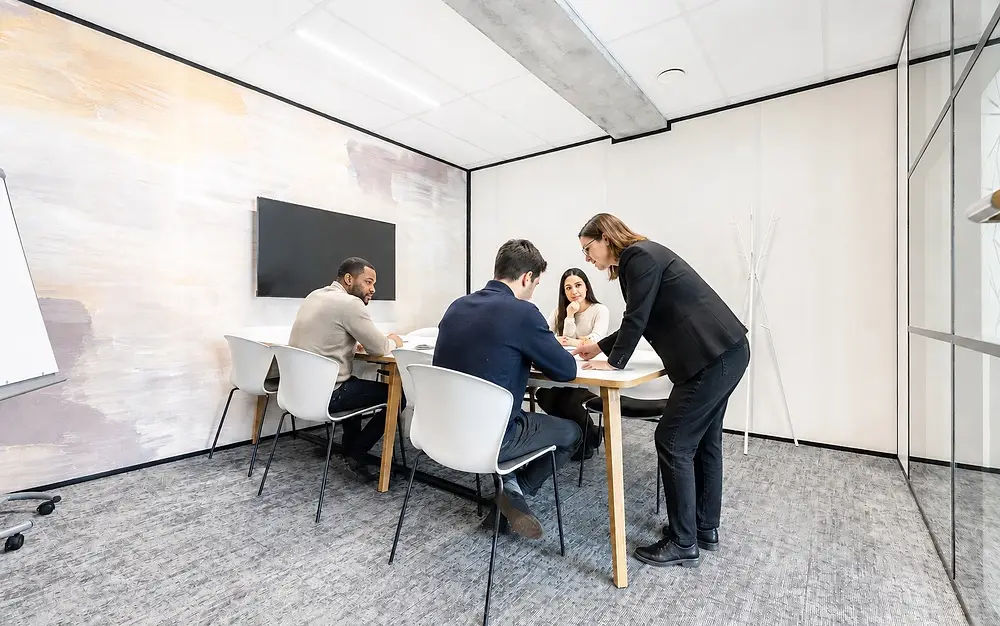 Une formatrice accompagne trois participants penchés sur un document, autour d'une table